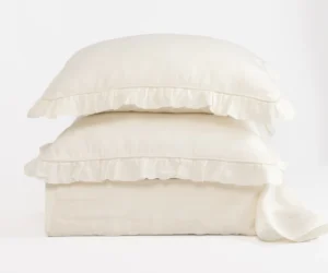 Three white pillows stacked on top of each other with ruffled edges against a white background