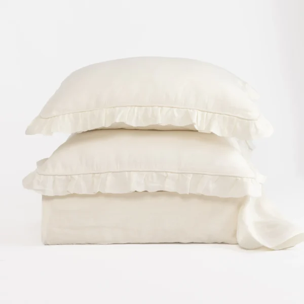 Three white pillows stacked on top of each other with ruffled edges against a white background.