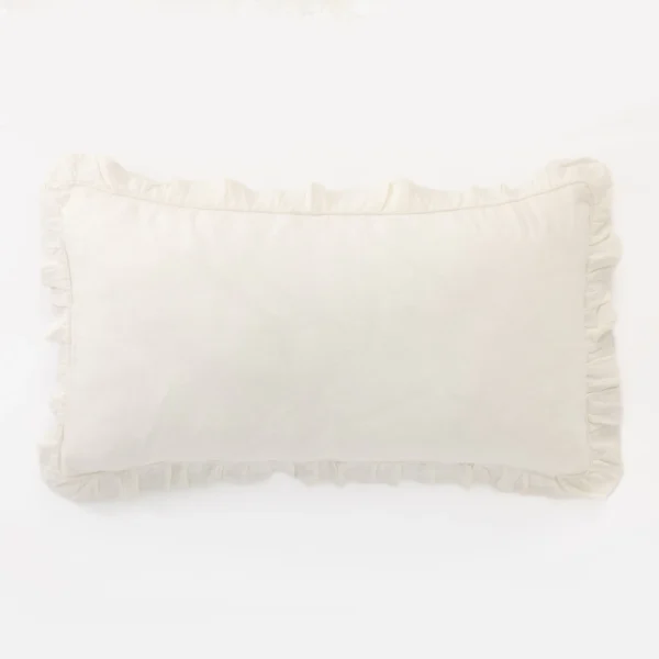 Light cream pillow with gathered edge resting on a white surface photographed against a pale backdrop