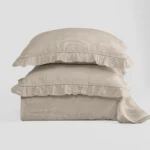 Stack of beige linen pillows with ruffled edges against a light background