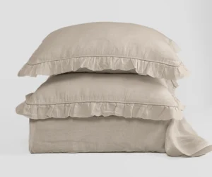 Stack of beige linen pillows with ruffled edges against a light background