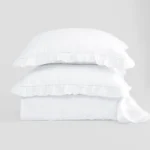 Stack of white pillows neatly stacked on a light grey background showcasing a soft bedding product