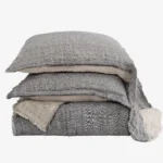 Stack of gray denim pillows with frayed edges stacked on a white background