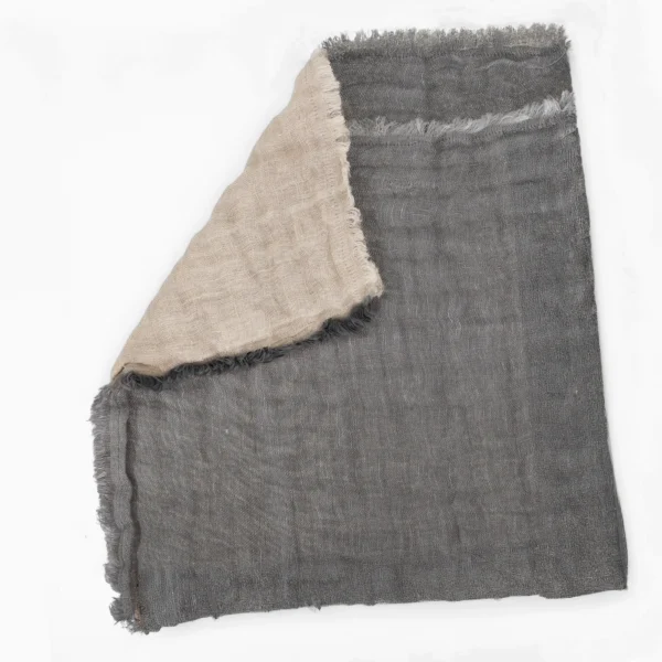 Close up of a dark denim fabric with a frayed edge folded under a light beige woven cloth