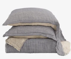 Stack of layered linen cushions in gray and beige with frayed edges on a pale background