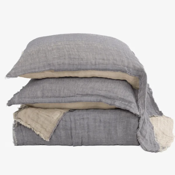 Stack of layered linen cushions in gray and beige with frayed edges on a pale background