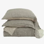 Stack of beige linen pillows with frayed edges stacked against a white background photographed up close