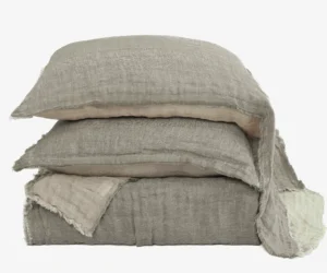 Stack of beige linen pillows with frayed edges stacked against a white background photographed up close