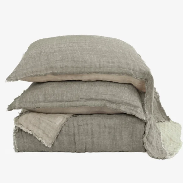 Stack of beige linen pillows with frayed edges stacked against a white background, photographed up close.