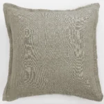 Beige linen throw pillow with frayed edges lying flat on a white surface
