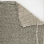 Close up of coarse beige burlap fabric with frayed edges laid over another fabric showing woven texture and natural fibers