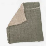 Gray woven fabric with frayed edges and a pale pink scarf draped over it shown in close up