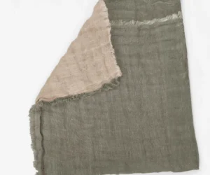 Gray woven fabric with frayed edges and a pale pink scarf draped over it shown in close up