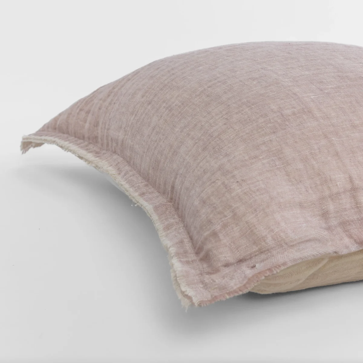 Close up of a dusty pink linen pillow with a frayed edge resting on a white surface showing the textured fabric weave