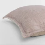 Close up of a dusty pink linen pillow with a frayed edge resting on a white surface showing the textured fabric weave