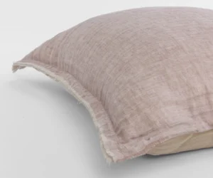 Close up of a dusty pink linen pillow with a frayed edge resting on a white surface showing the textured fabric weave