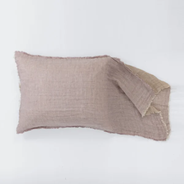 Soft pink pillow with frayed edges lying on a white surface across the bottom of the image with a second overlapping piece nearby