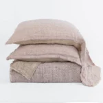 Stack of several light beige linen pillows with frayed edges arranged against a white backdrop showcasing soft textured fabric