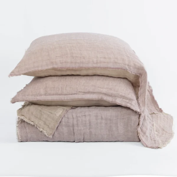 Stack of several light beige linen pillows with frayed edges arranged against a white backdrop, showcasing soft textured fabric.