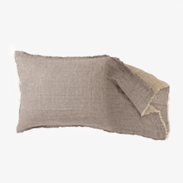 Beige linen throw pillow with frayed edges lying on a light background stacked with another pillow nearby