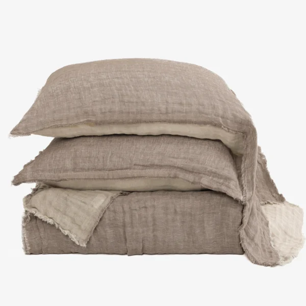 Stack of beige linen pillows with frayed edges arranged in a tower against a white background, textured fabric visible.