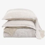 Stack of beige linen throw pillows with frayed edges against a white background arranged in a tower