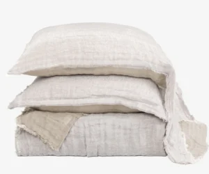 Stack of beige linen throw pillows with frayed edges against a white background arranged in a tower