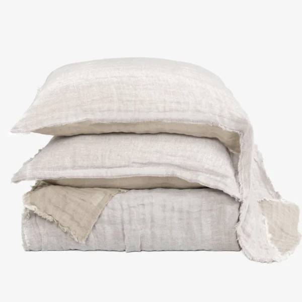 Stack of beige linen throw pillows with frayed edges against a white background, arranged in a tower.