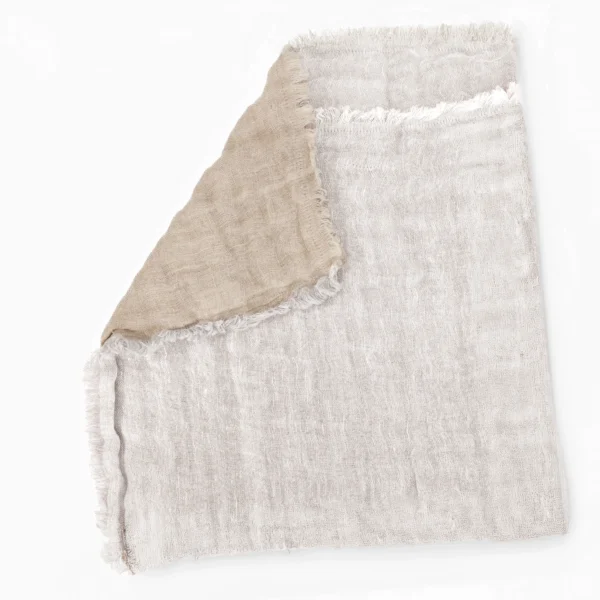 Beige woven blanket with frayed edges laid flat on a white background