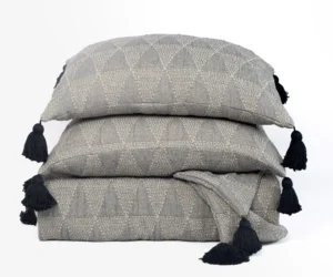 Stack of gray patterned throw pillows with dark tassels at the corners arranged in a neat pile
