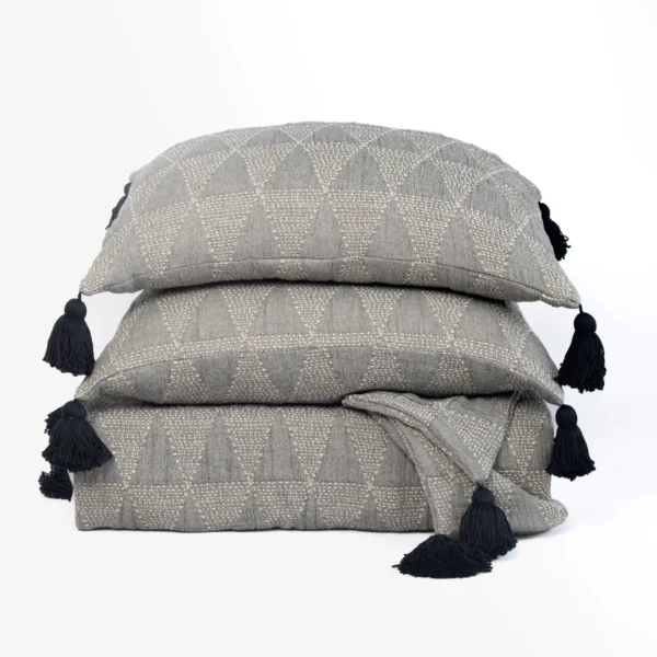 Stack of gray patterned throw pillows with dark tassels at the corners, arranged in a neat pile.