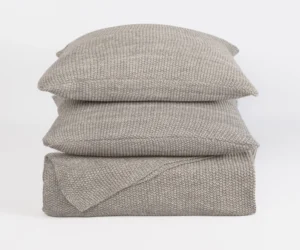 Stack of light gray knitted throw pillows stacked on a white background with a chunky knit pattern
