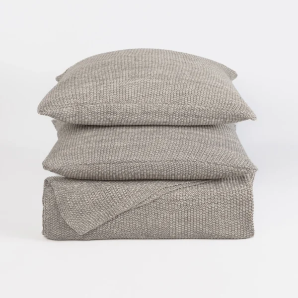 Stack of light gray knitted throw pillows stacked on a white background with a chunky knit pattern