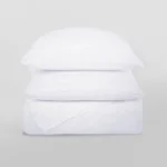 Stack of white knitted pillows stacked in a tall column against a light gray background showcasing textured fabric