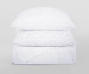 Stack of white knitted pillows stacked in a tall column against a light gray background showcasing textured fabric
