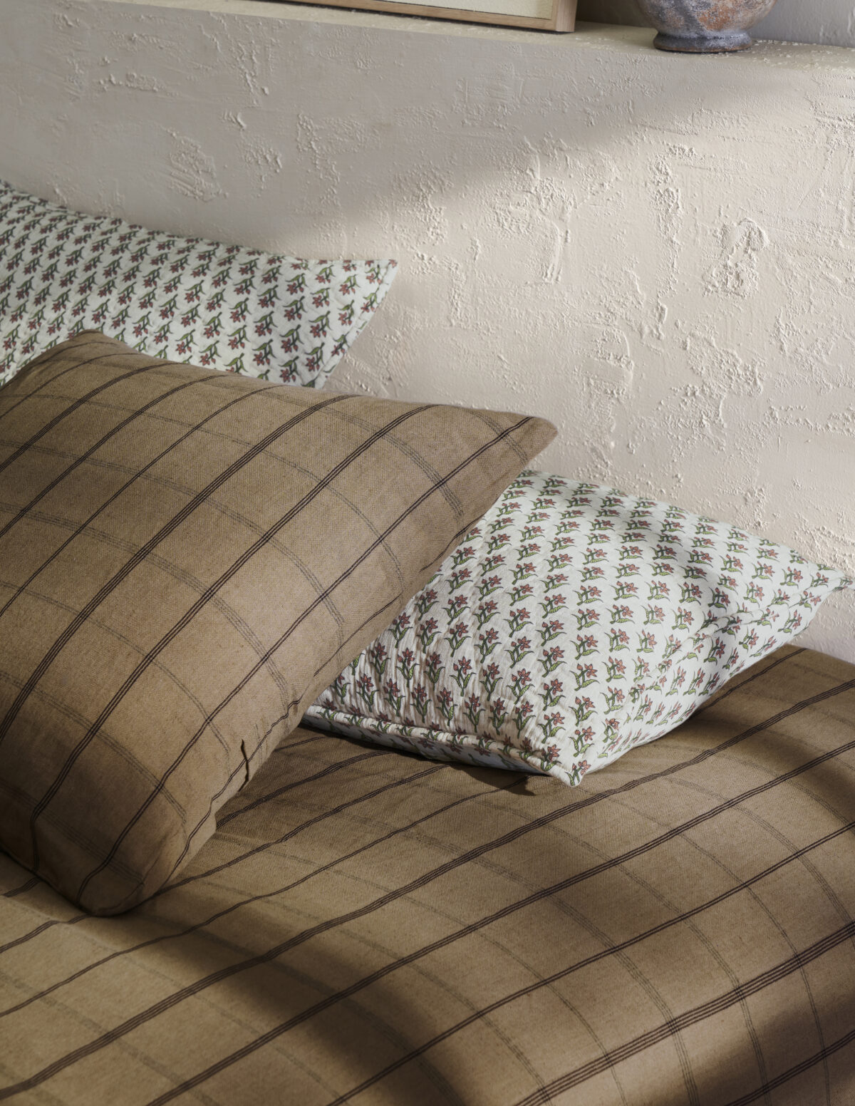 Two decorative pillows on a brown striped sofa a tan striped pillow in front and a white floral patterned pillow behind it