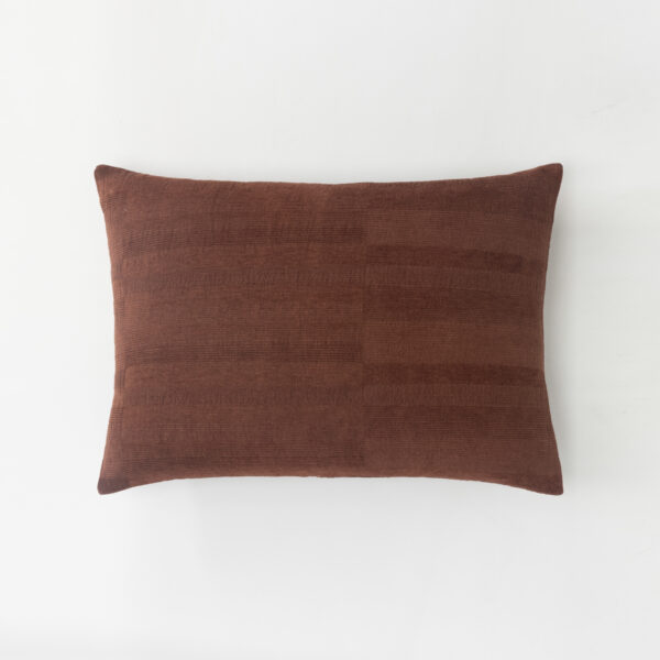 Brown textured throw pillow on a white surface viewed from the side partial view