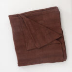 Folded brown corduroy blanket resting on a white surface showing its textured fabric and edges