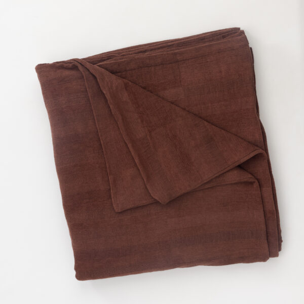 Folded brown corduroy blanket resting on a white surface showing its textured fabric and edges