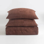 Three brown textured pillows stacked on a white surface viewed from the side creating a cozy cushion tower