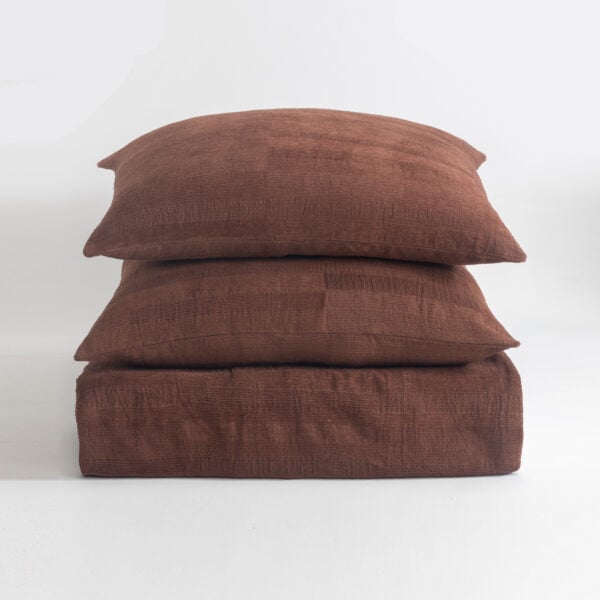 Three brown textured pillows stacked on a white surface, viewed from the side, creating a cozy cushion tower.