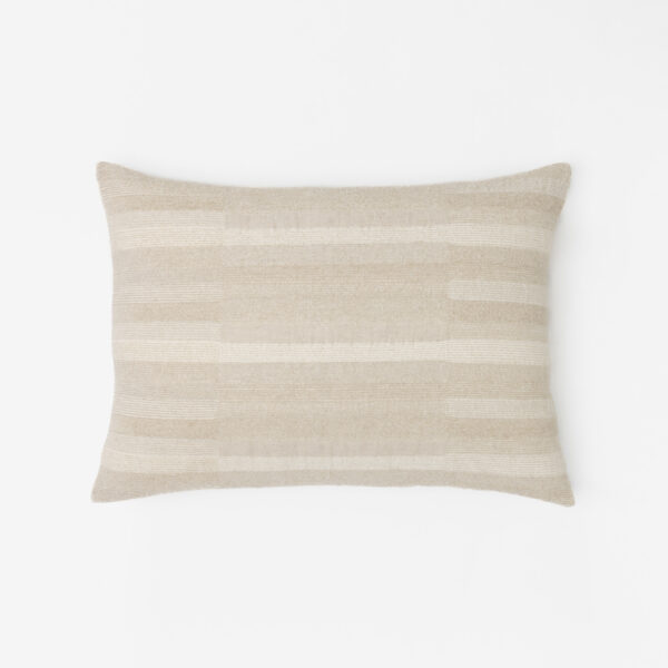 Beige striped pillow resting on a white surface photographed from the side to show its texture and shape