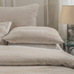 Close up of beige cushions on a bed with a soft toned headboard and a lamp on the right side table Buttery neutral tones and plush textures dominate the scene