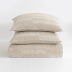 Stack of three beige textured throw pillows stacked on a white surface httpsexample Com