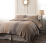 Neutral toned bedroom with a made bed beige duvet and matching pillows a round sunburst mirror hangs above the headboard and a bedside table with a lamp sits to the right in soft light