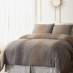 Bed with a brown blanket and beige pillows a sunburst mirror hangs on the light wall above the headboard