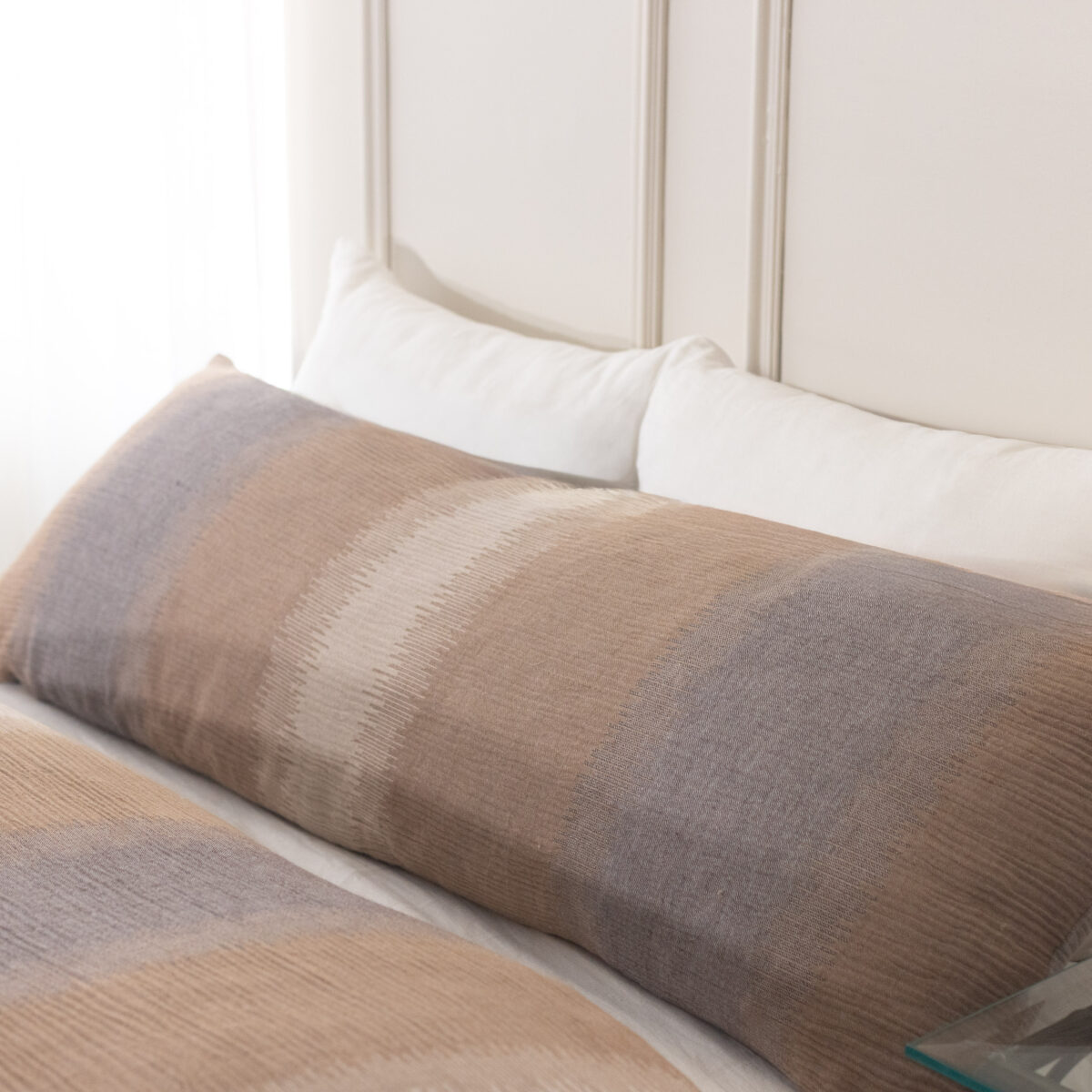 Close up of a neatly made bed with white pillows and a beige brown striped blanket against a light headboard