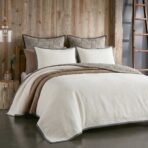 Rustic bedroom scene with a bed neutral bedding and a wooden paneled wall a ladder is visible on the right side
