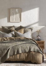 Bed with layered quilted bedding and patterned pillows against a textured wall framed geometric art hangs above