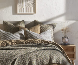 Bed with layered quilted bedding and patterned pillows against a textured wall framed geometric art hangs above
